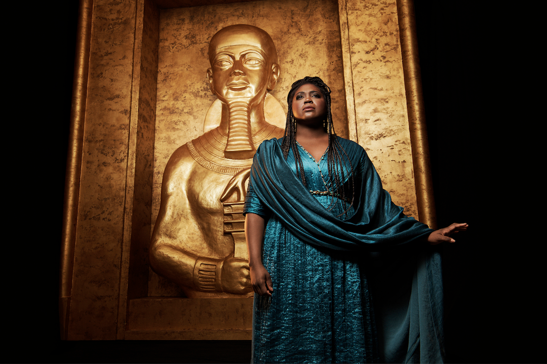 Black woman in a vibrant blue dress standing in front of a gold statue