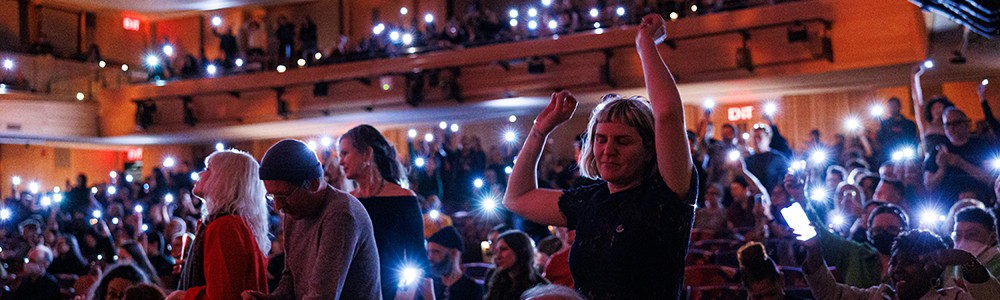 A woman dances in a crowd as people hold up phone lights