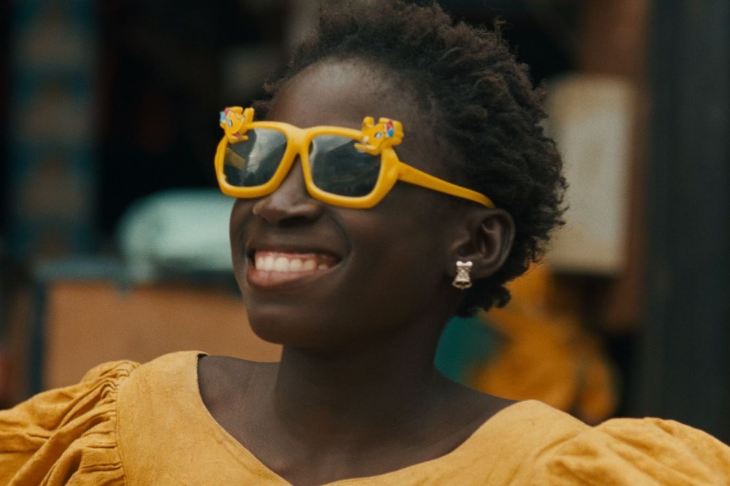 A black woman with short brown hair wearing orange sunglasses and an orange shirt