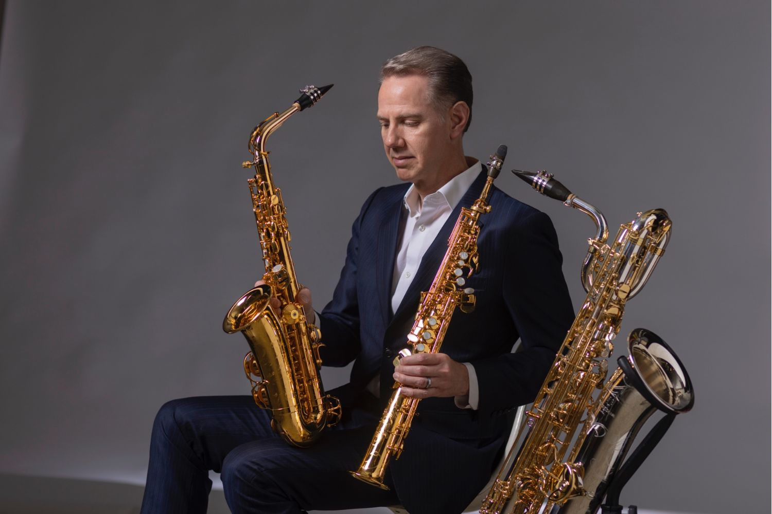 A man in a suit holding three different sized saxophones 