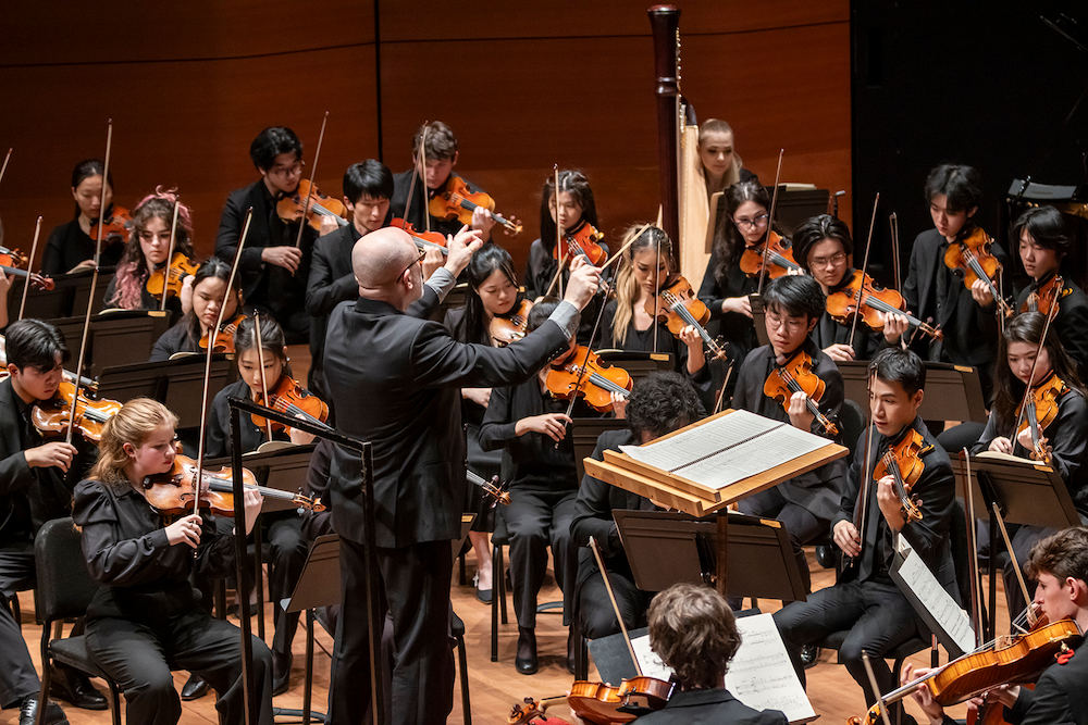A man in a yellow t-shirt laying on his side in front of a projected version of Hamlet