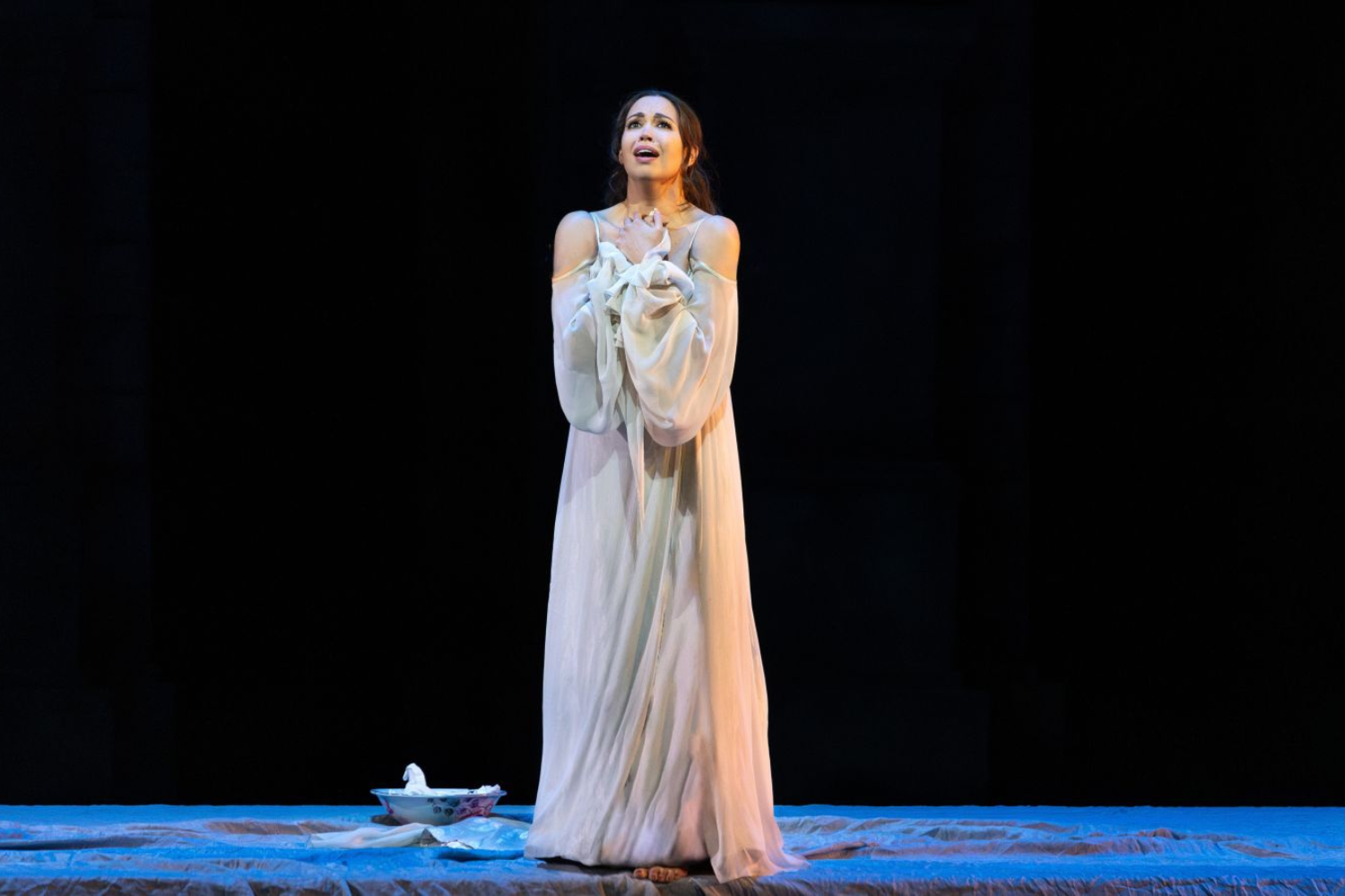 A woman with blonde hair wearing a white dress lying on a marble slab