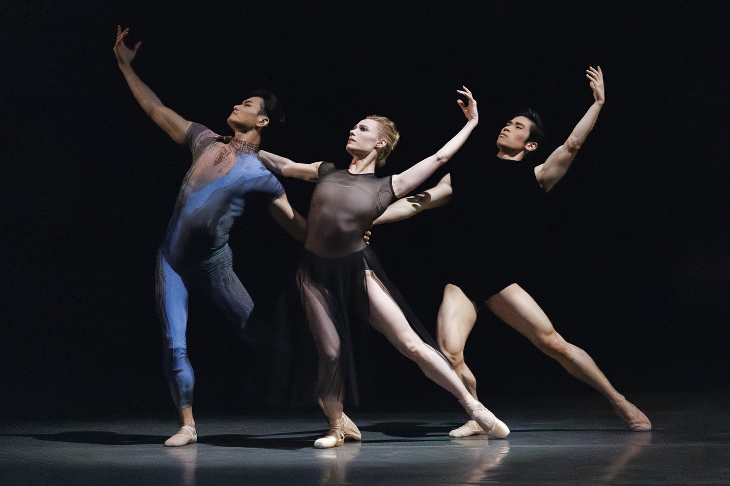 Three dancers in leotards on a dark stage 