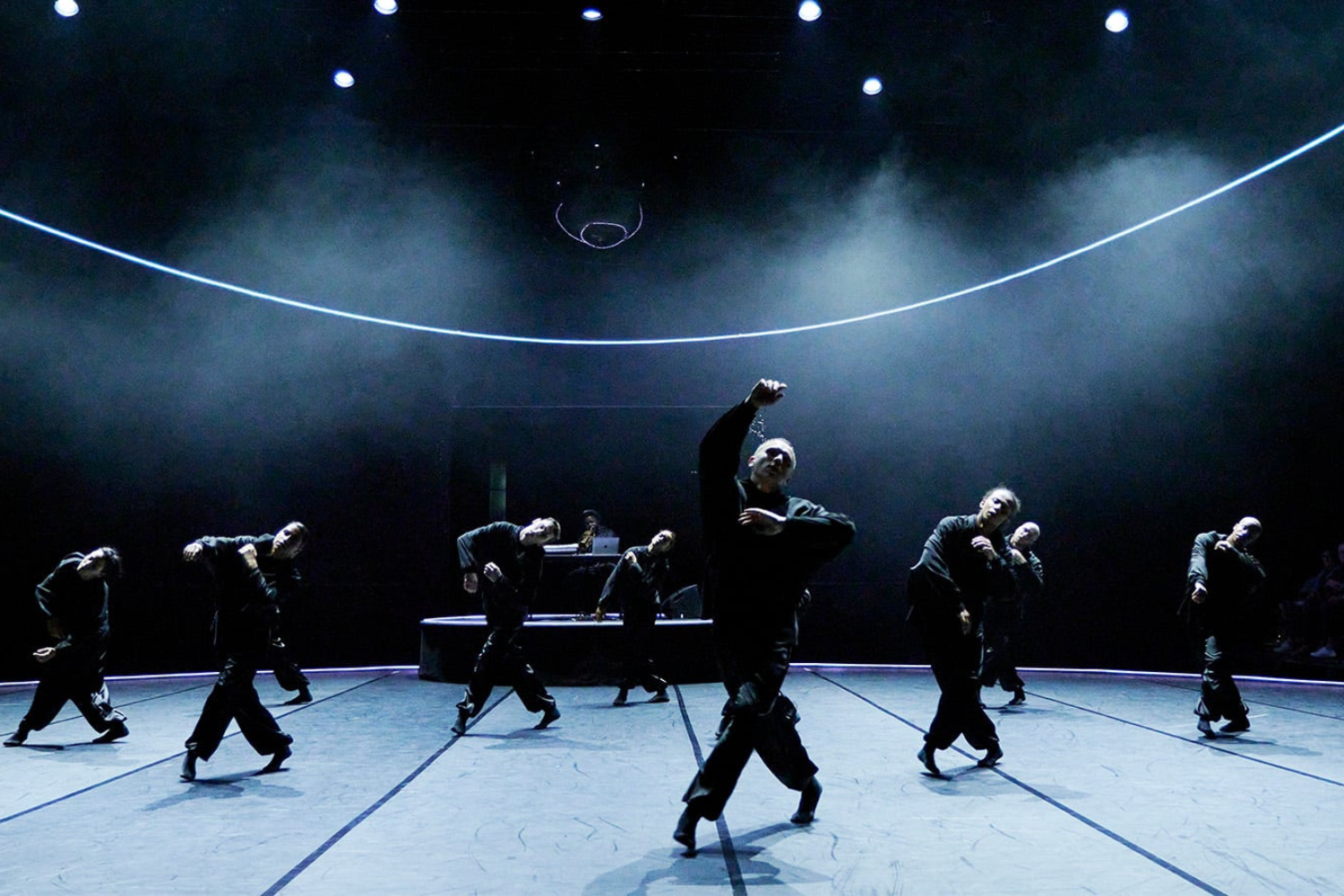 A group of dancers in all black on a dark stage