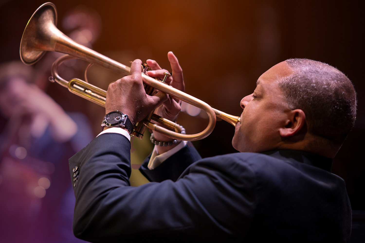 A black and white photo of a woman with dark curly hair in front of a pink and blue graphic