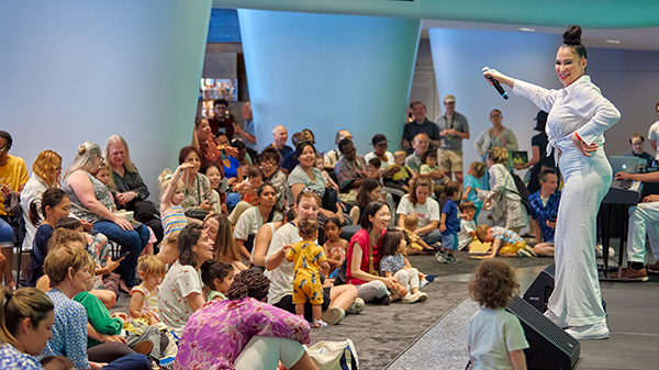 Kids and parents sit on the floor in front of a performer on stage