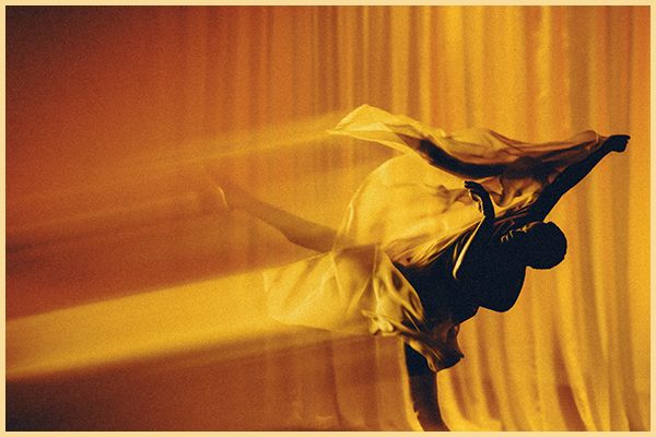 A dancer moves against a gold curtain