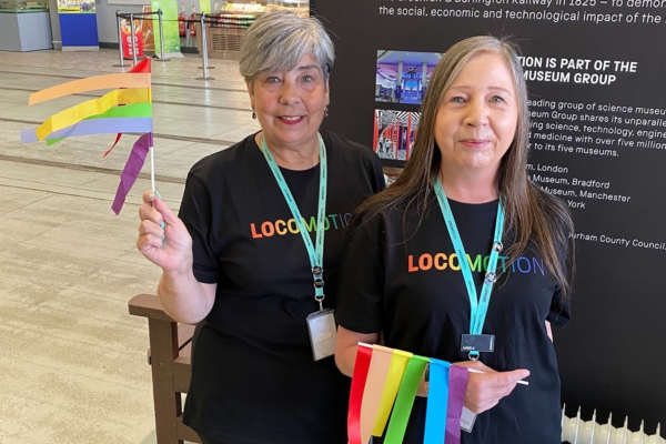 Two Locomotion colleagues wearing black t-shirts with 'Locomotion' written on them in rainbow colours holding rainbow streamers