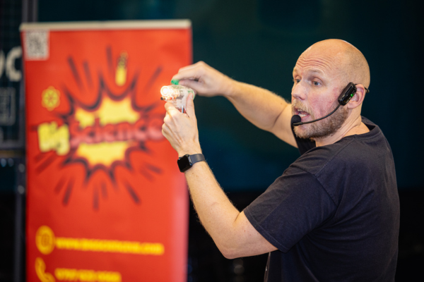 A man in a black t-shirt delivering a talk to visitors