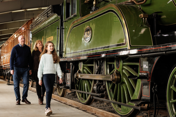 An older couple and child walking past a green steam engine
