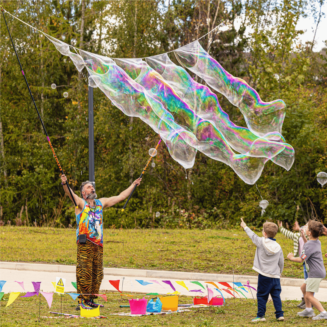 Giant bubbles being created by a man in a rainbow top and animal-print trousers