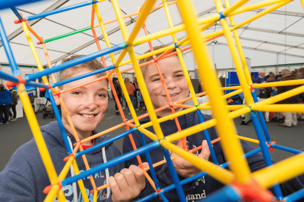 Two boys in blue hoodies standing looking through a structure made from K'nex