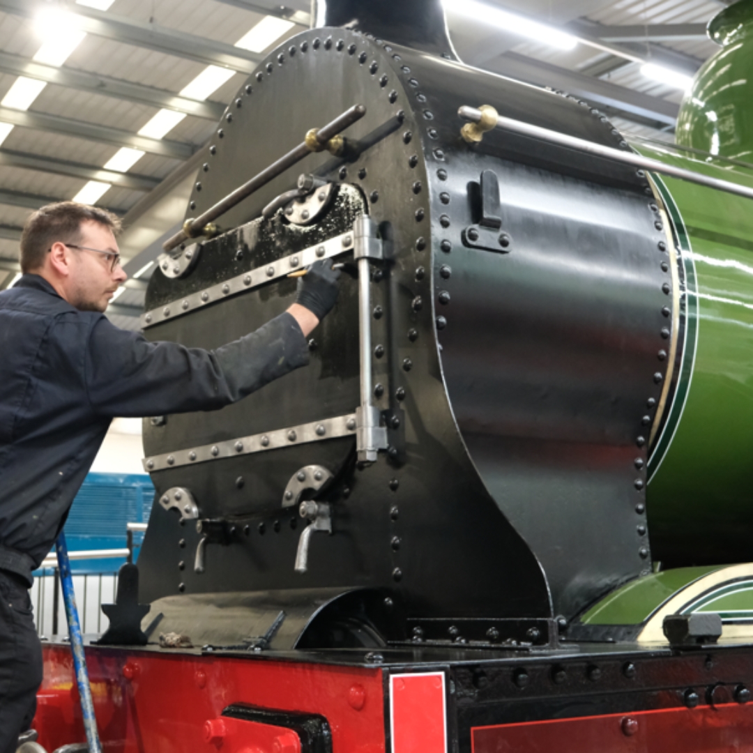 A man in a blue boiler suit painting a green steam engine