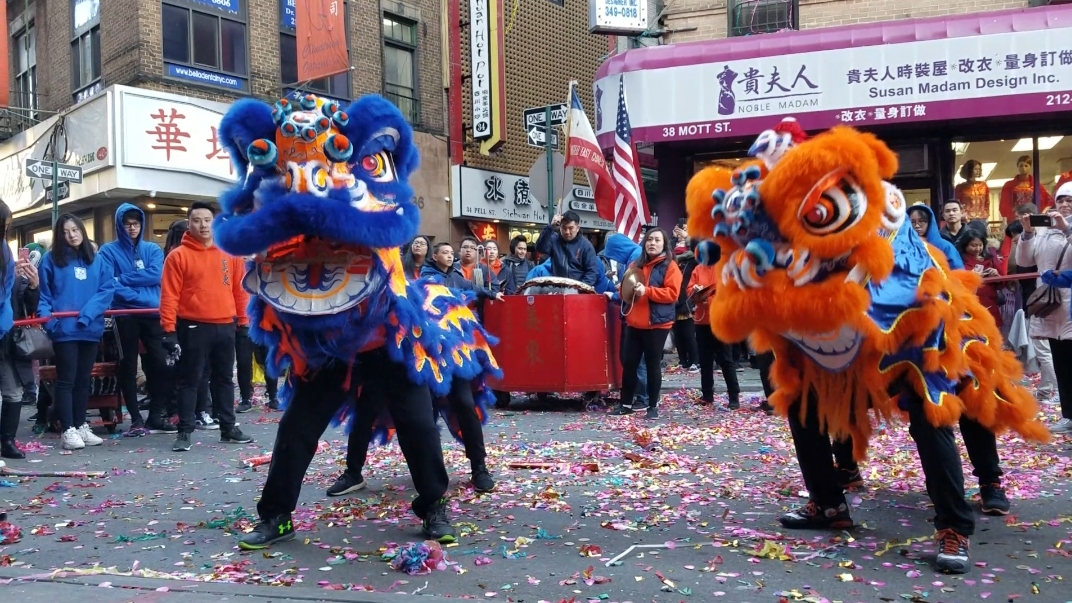 A blue and orange lion dancing in the streets of Chinatown