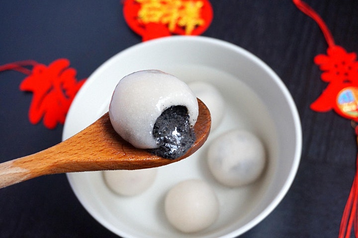 A spoon with a tang yuan that has been opening to show the delicious black sesame filling.