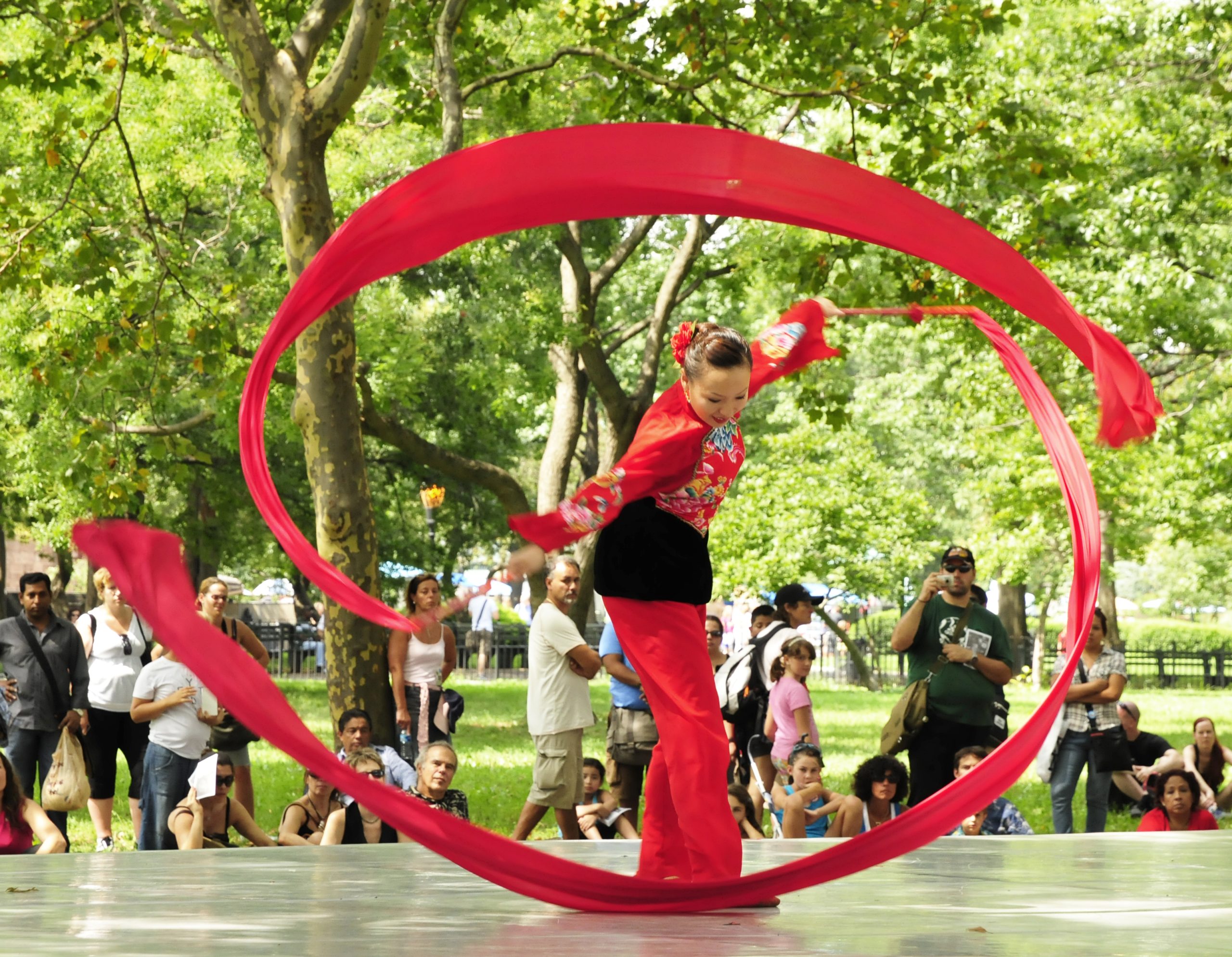 A dancer twirls two long red ribbons in a graceful circle.