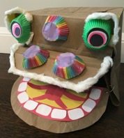 A stylized lion head made of a paper bag, colored paper, and muffin wrappers.