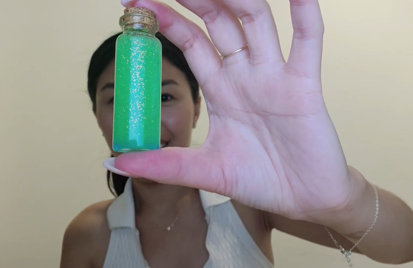 A hand holding a tube with a mysterious green sparkly liquid inside