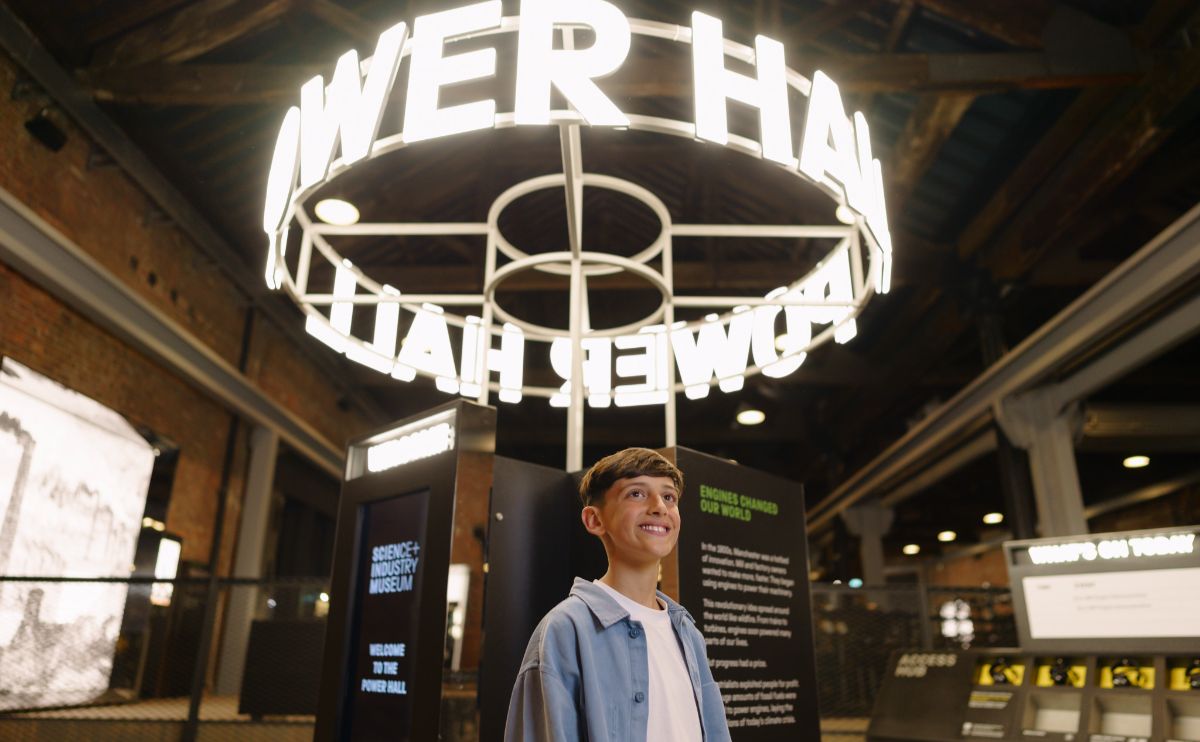 A young boy stood below a bright lit up Power Hall sign