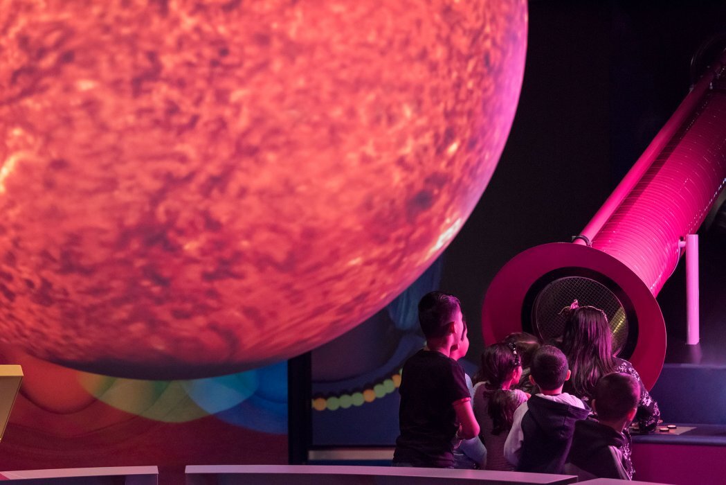 A planet hovers in the foreground as children look at an exhibit.
