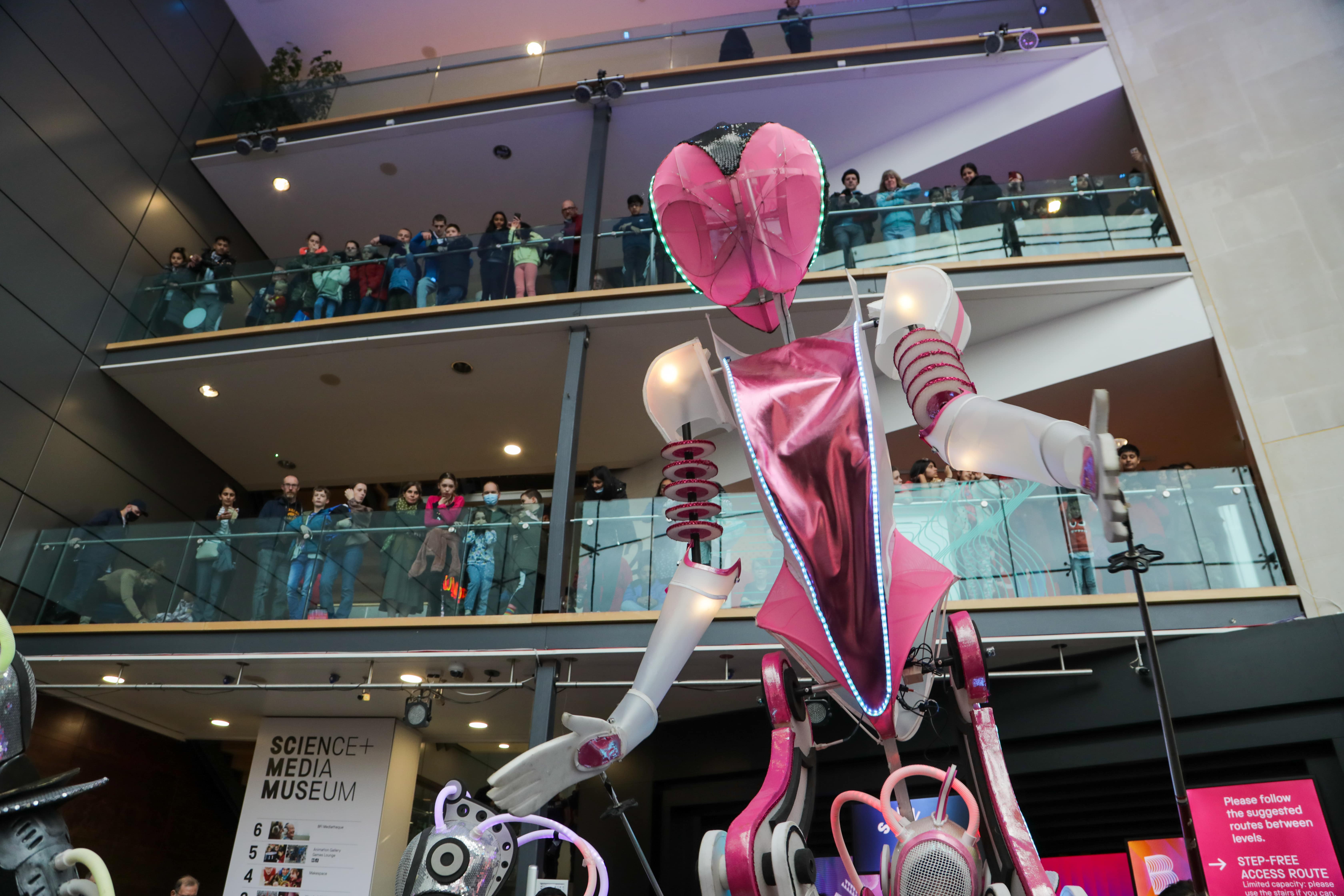 A giant pink and white puppet looms large in the foyer of the National Science and Media museum, with people looking down from the balconies.