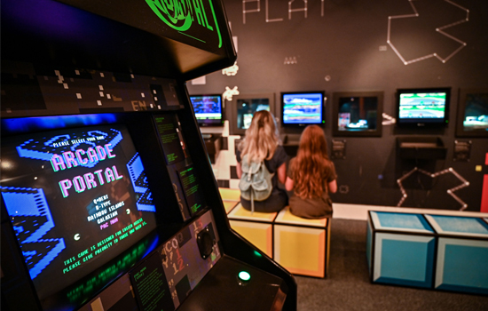 A close up of the Arcade Portal game in Games Lounge, in the background a woman and young girl play on one of the videogames.