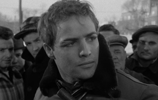 A black and white image of Marlon Brandon looking pensive with a crowd behind him