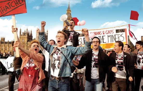 A group of young people from Lesbians and Gays Support the Minders marching in London, fists raises, shouting and cheering.