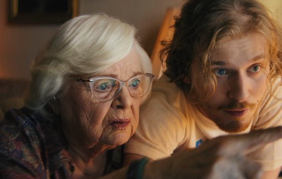 An old woman and a man in his 20s stare at a computer screen in an inquisitive manner