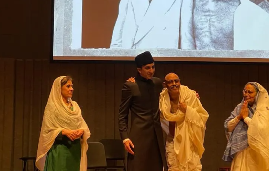 Two women actors, dressed in Saris, look on at two men who are dressed as Gandhi and Jinnah. Behind them, a photograph of the real Gandhi and Jinnah.