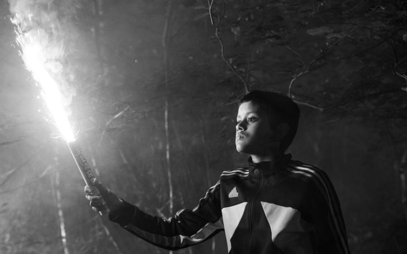 A black and white image of a boy in a tracksuit holding a flare