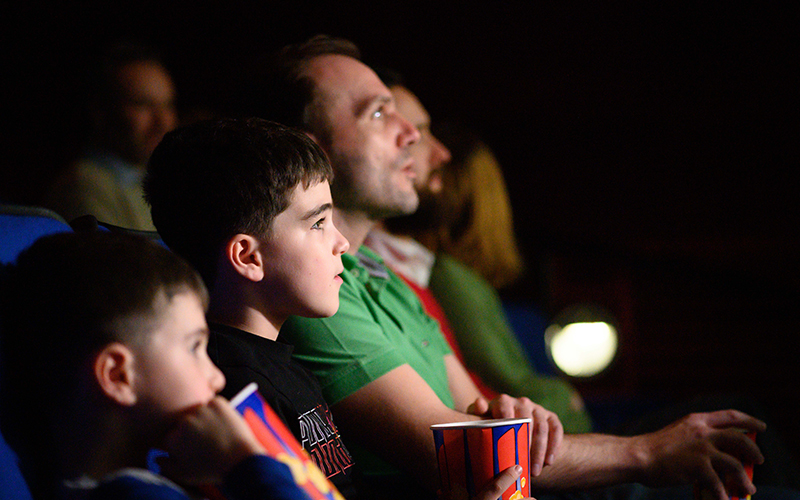 A family consisting of a dad and two young boys watching a film with popcorn