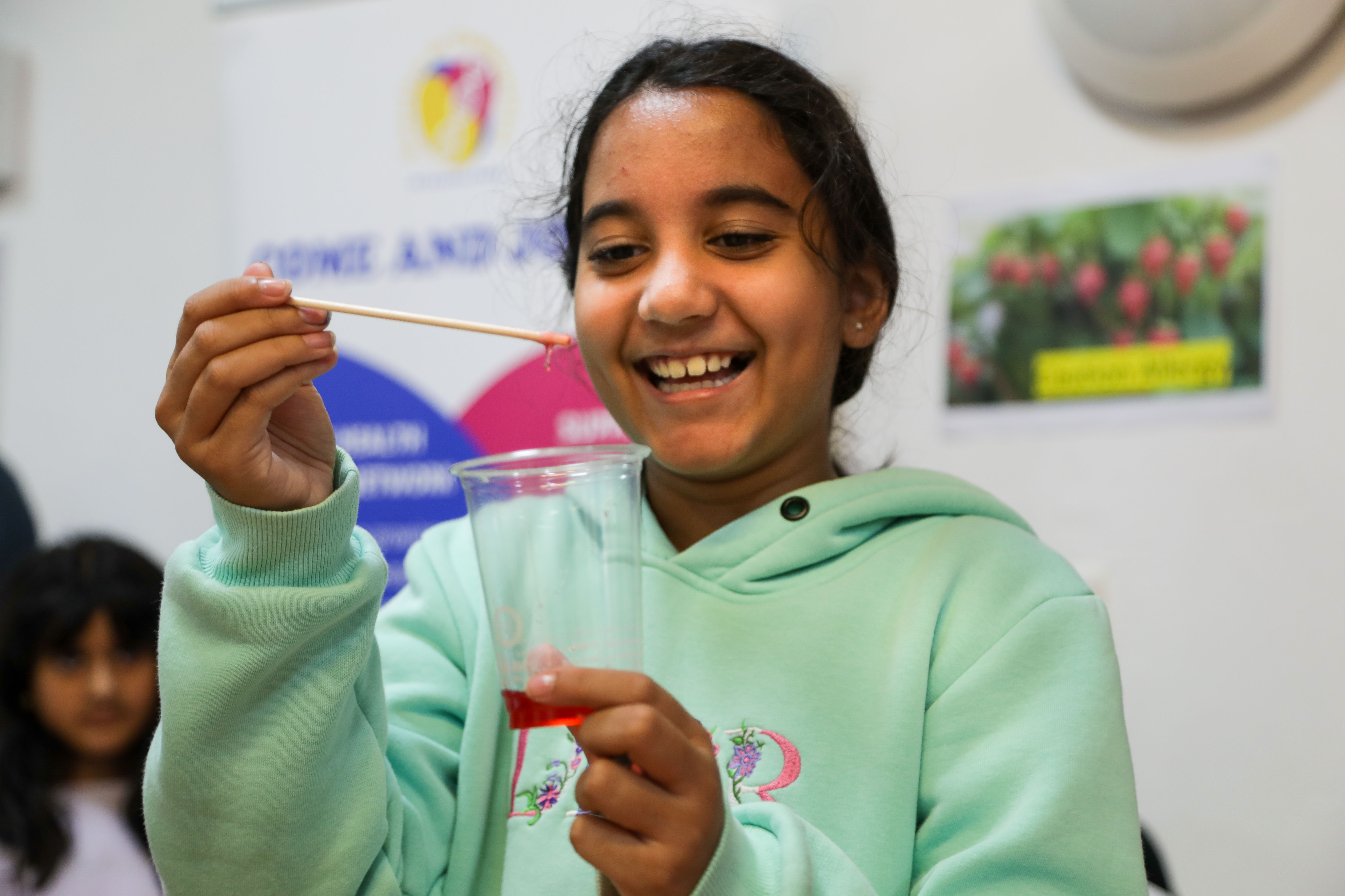 A young girl in a turquoise hoody looking at a cup of red gooey liquid