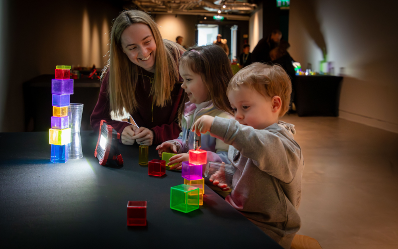 A mum and two young children play with colourful blocks
