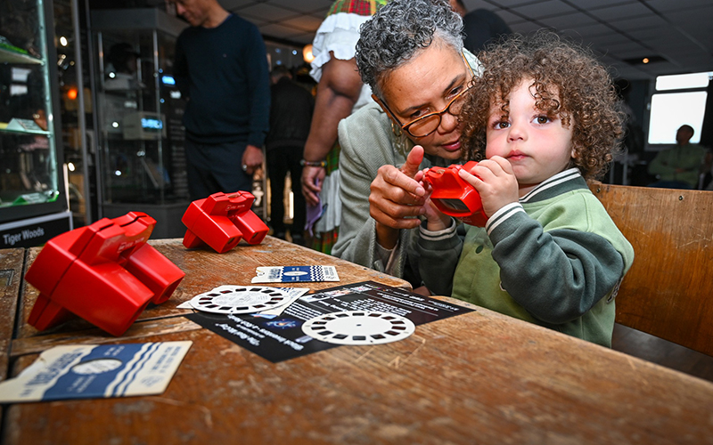 A woman and a young child holding red view-master glasses, a form of stereoscope for looking at slides.