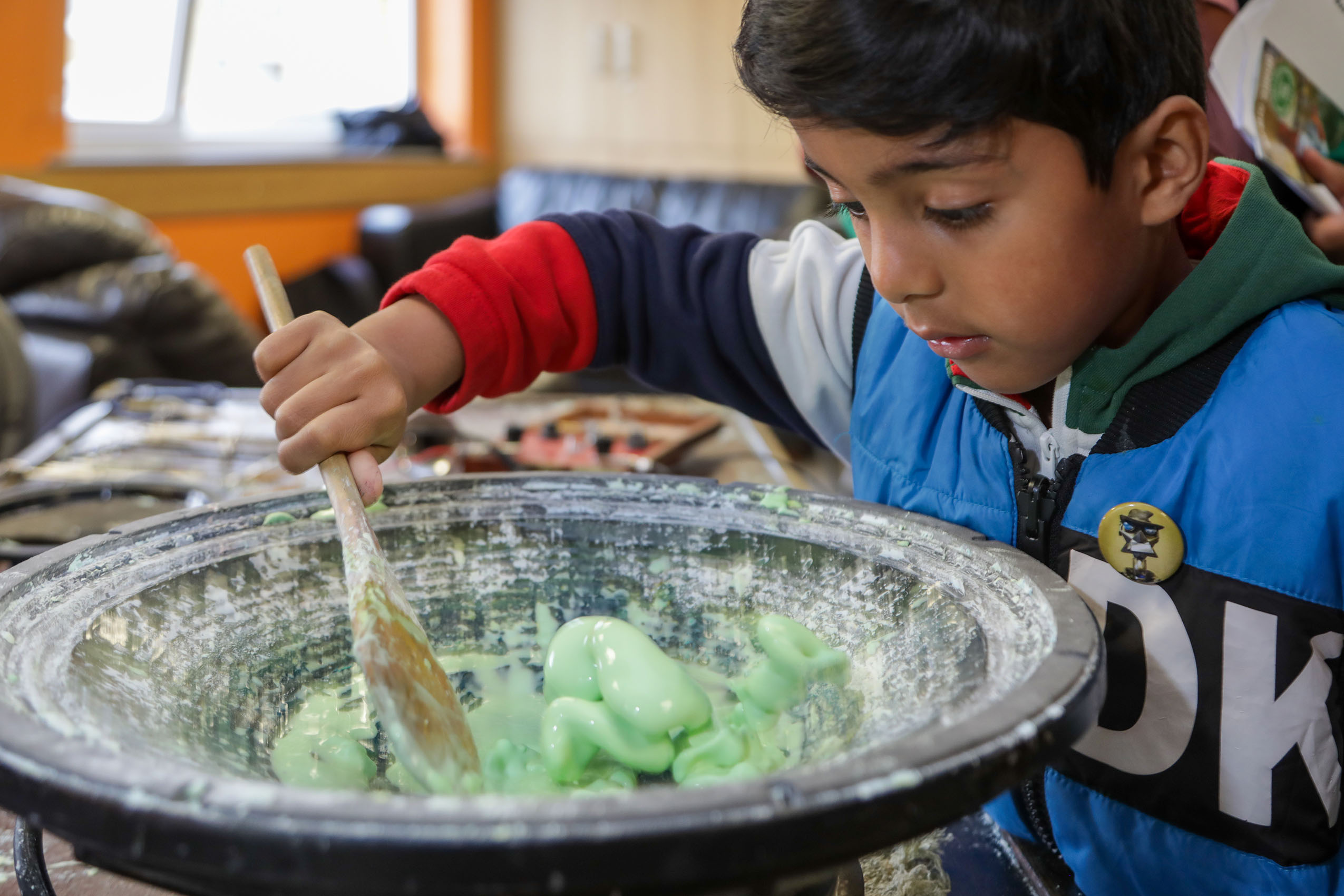 A young boy stirs green slime with a wooden spoon