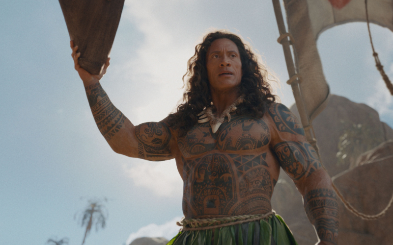 Still from the live action Moana. A heavily tattooed Polynesian demi god stands holding a piece of wood.