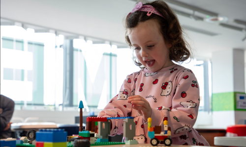 A young girl wearing a pink Hello Kitty jumper creates scenes with Lego.