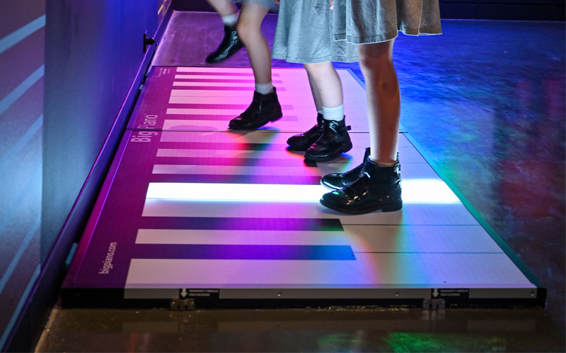 Children's feet playing on a large, light-up piano in Wonderlab Live