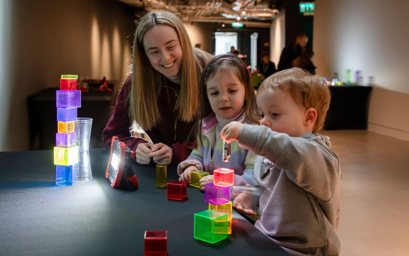 A mum and two young children play with colourful blocks