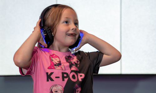 A child smiling with silent disco headphones on and wearing a KPOP tshirt