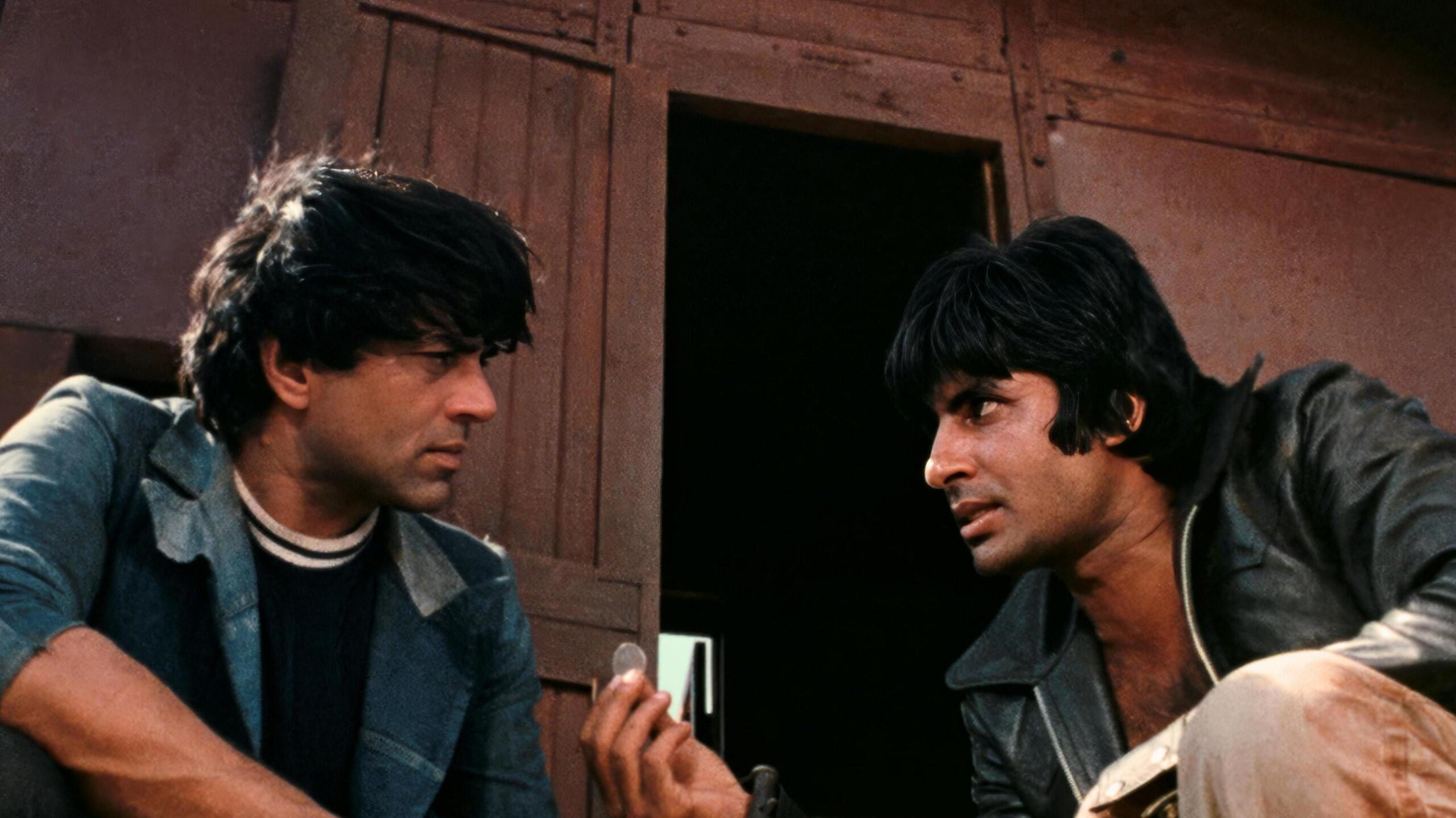 Two men sit in front of a rustic building. One hold a coin ambiguously. Their expressions are serious, conveying a moment of tension or decision.