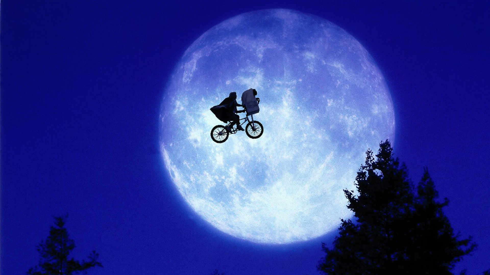 Image from E.T.; A young boy rides a flying bike in front of large full moon, in the basket of the bike is a small alien covered by a blanket
