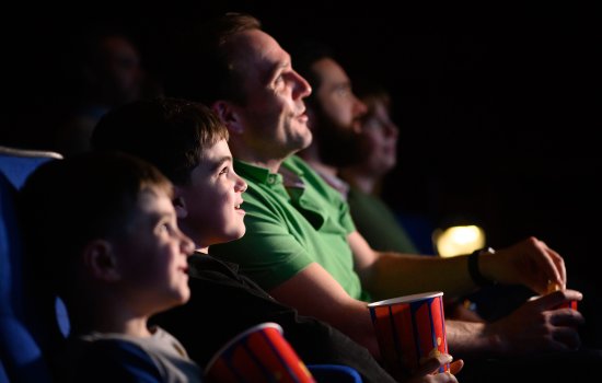 A family sit in a cinema smiling.