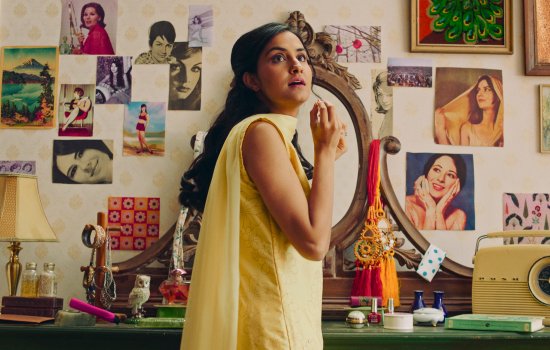 A woman stands in front of a dresser, gazing in wonder off-screen.