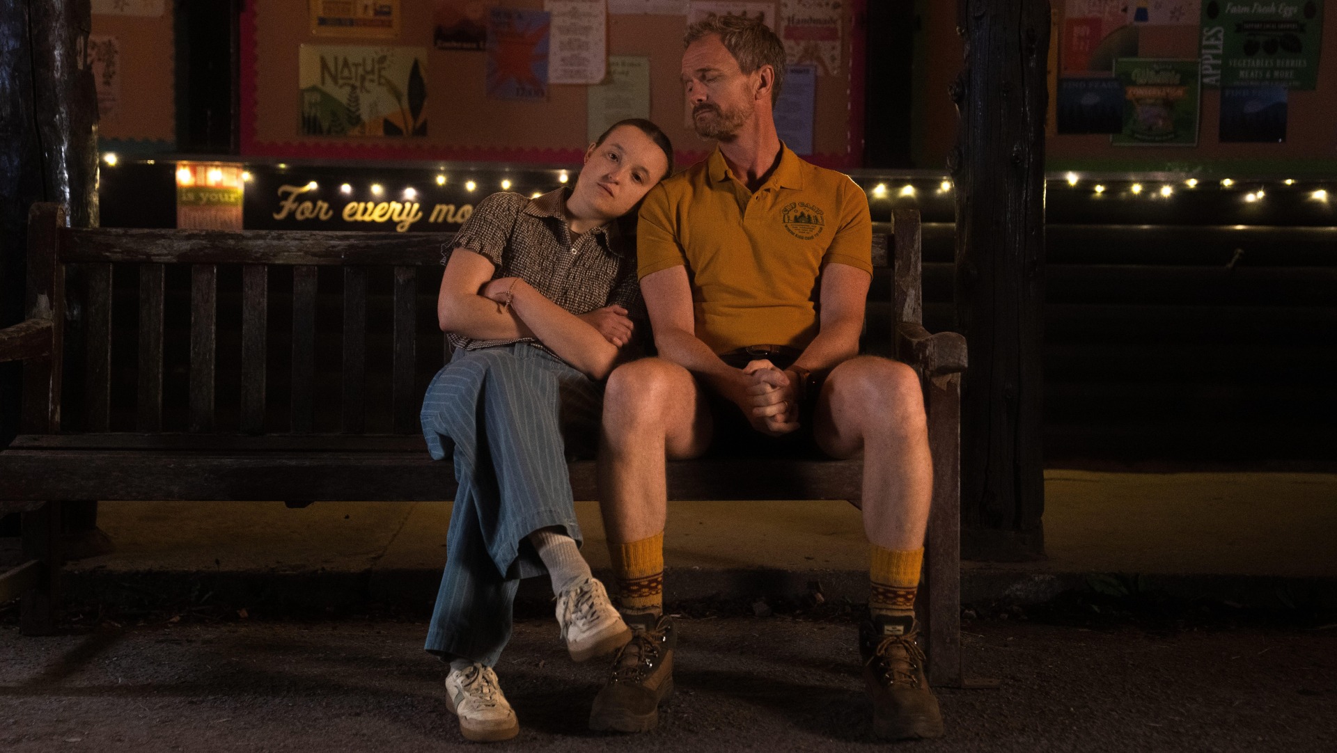 Bella Ramsay sits next to Neil Patrick Harris with their head on his shoulder.