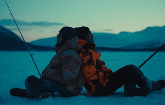 Two men sit back to back, fishing in an icy landscape.