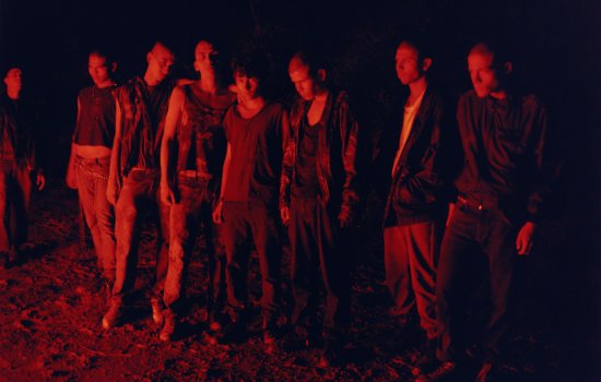 A group of teens stand together in the dark, lit by a dull red lght
