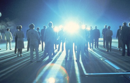 A group of people stare at a very bright light looming over the horizon