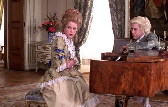 A man and woman sit by a piano, dressed in period costume.